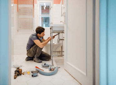 A Photograph of a Man Installing Piping For a Sink Beside a Toilet